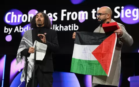 El director sirio-palestino Abdallah Alkhatib ofrece un discurso mientras el productor argelino Taqiyeddine Issaad sostiene una bandera palestina.