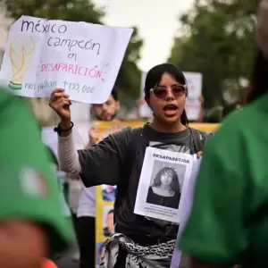 Una integrante del colectivo "Madres Buscadoras" sostiene un cartel de protesta mientras marcha hacia el Estadio Azteca antes de la apertura.